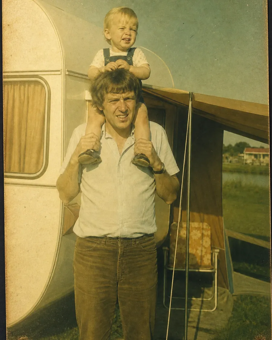 Kiekje uit 1979: een jonge vader met een peuter op zijn schouders naast een caravan, de afdruk geel geworden en aan één kant verbleekt.