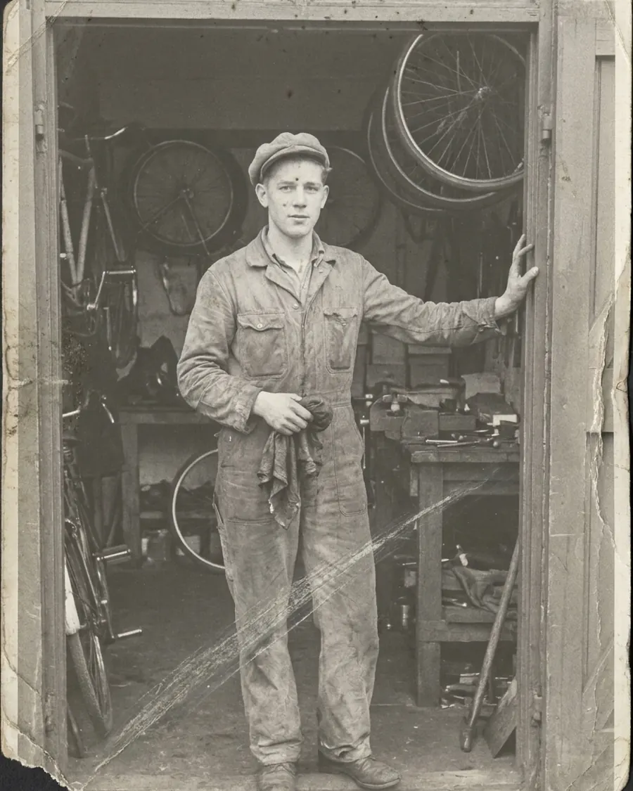 Foto uit 1958: een man van vierentwintig in overall in de deur van een fietsenwinkel, de afdruk versleten, vlekkerig en met een afgescheurde hoek.