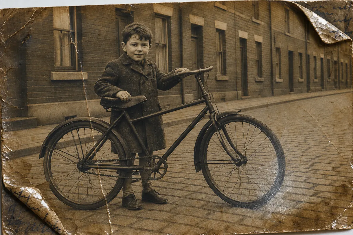 Kinderfoto uit 1952: een jongen in een wollen jas naast een zware fiets in een straat met keien en rijtjeshuizen; over de afdruk staat pengekrabbel en de hoeken zijn omgevouwen.
